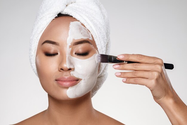 Young lady with towel on head put scrab on her face isolated