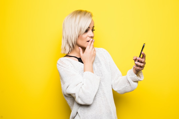 Young lady woman girl in white sweater uses smartphone on yellow