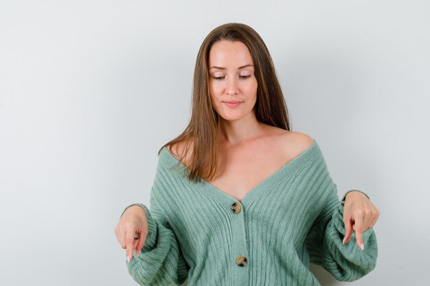 Young lady in wool cardigan pointing down and looking careful , front view.