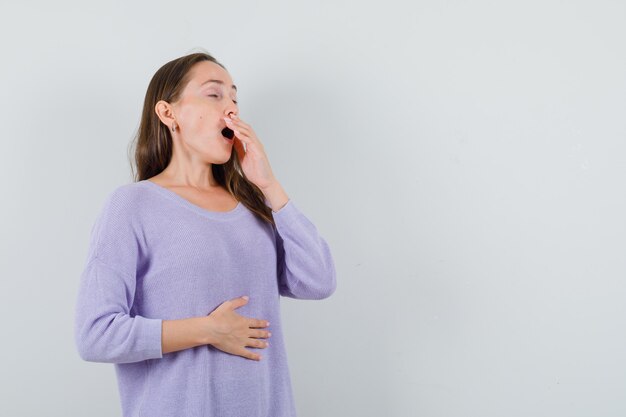 Young lady yawning in casual shirt and looking sleepy. front view.