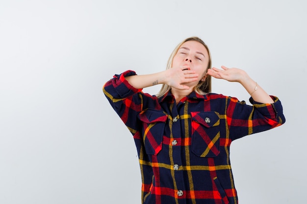 Young lady yawning in checked shirt and looking sleepy. front view.