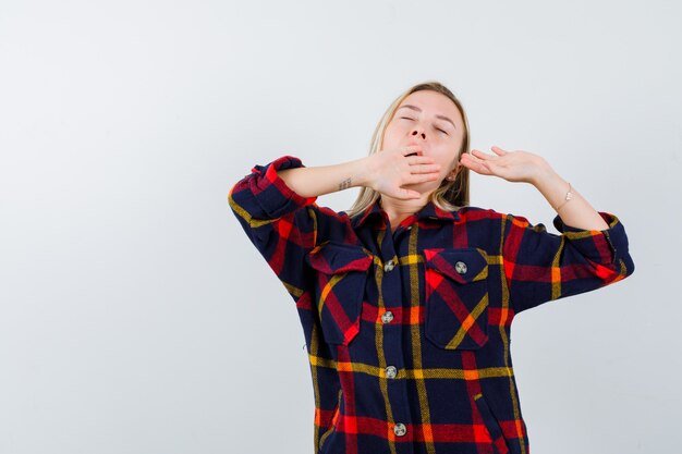 Young lady yawning in checked shirt and looking sleepy. front view.