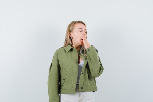Young lady yawning in jacket, pants and looking sleepy. front view.