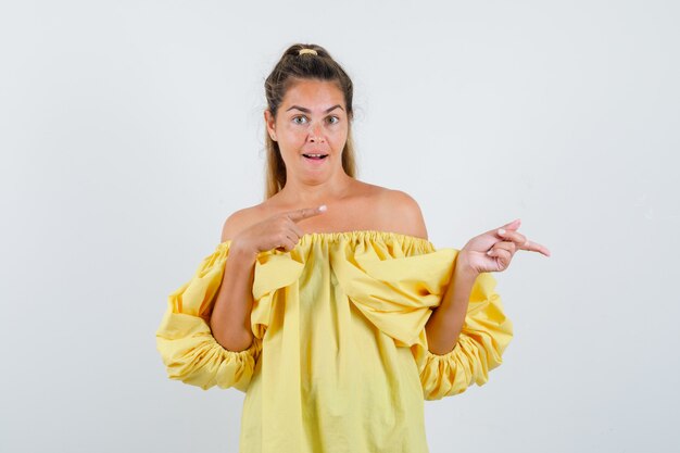 Young lady in yellow dress pointing to the right side and looking amazed, front view.