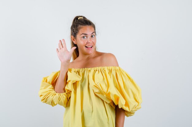 黄色のドレスを着た若い女性が挨拶と陽気に手を振って、正面図。