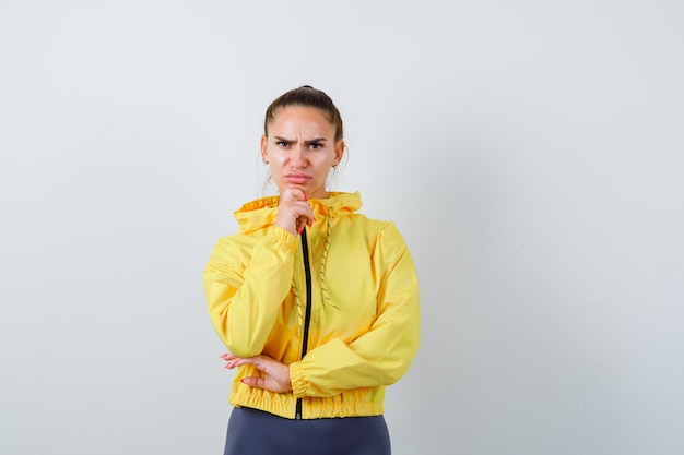 Young lady in yellow jacket propping chin on hand and looking serious , front view.