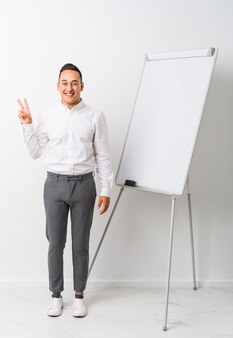 Young latin coaching man with a whiteboard isolated joyful and carefree showing a peace symbol with fingers.