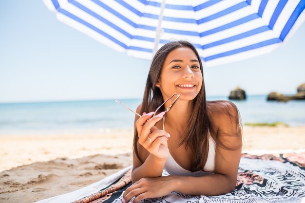 바다 해변에 태양 우산 아래 모래에 누워 젊은 라틴 여자. 여름 직업