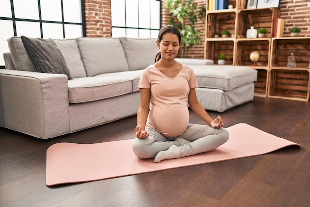 Young latin woman pregnant smiling confident training yoga at home