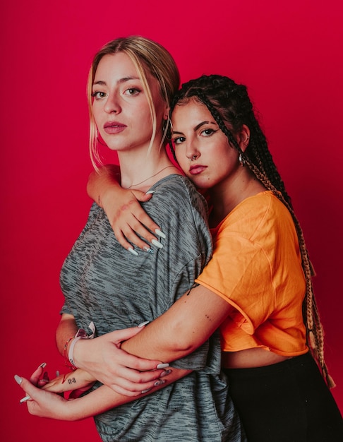 Young lesbian couple hugging each other on a red wall