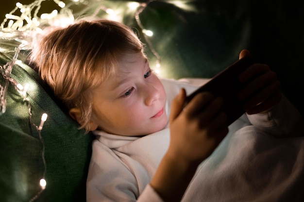 Free photo young little boy using smartphone in bed at night