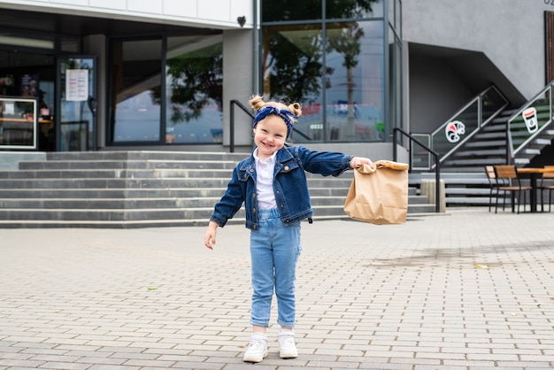 Young little girl with fast food bag near cafe outdoors