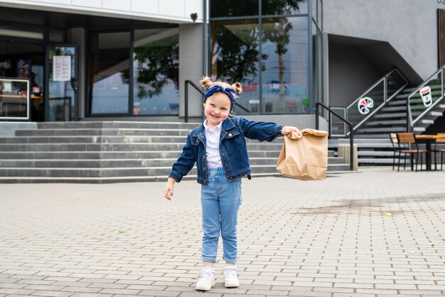 屋外のカフェの近くにファーストフードバッグを持つ少女