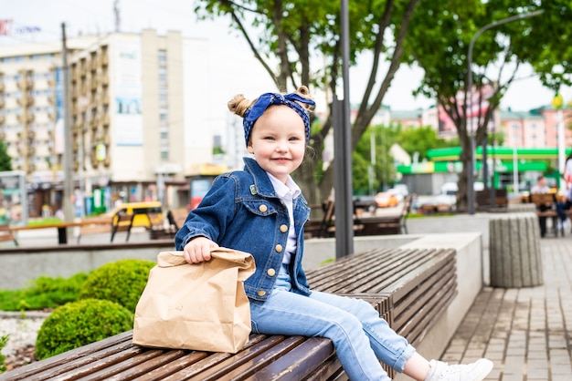 ベンチに座っているカフェの近くにファーストフードバッグを持つ少女