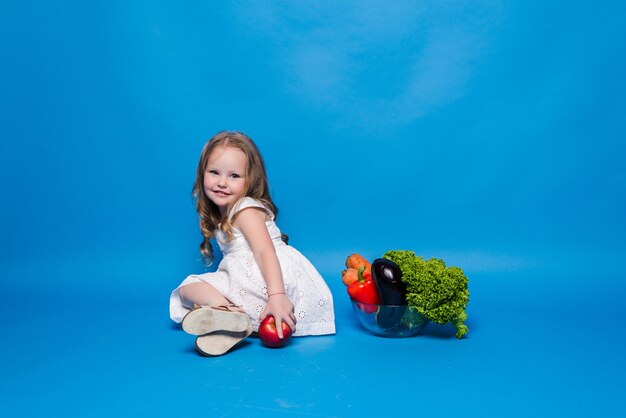 Young little girl with vegetables on a blue wall