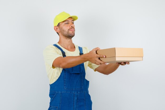 Young loader delivering cardboard box in uniform , front view.