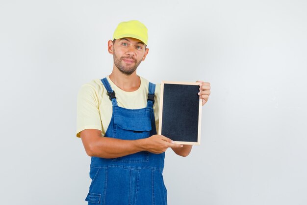 Young loader holding blackboard and smiling in uniform , front view.