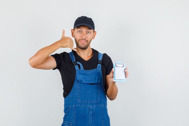 Young loader holding mini clipboard with phone gesture in uniform , front view.