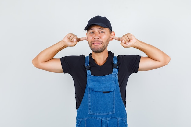 Free photo young loader plugging ears with fingers in uniform and looking annoyed , front view.