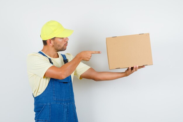 Young loader pointing at cardboard box in uniform and looking focused. front view.