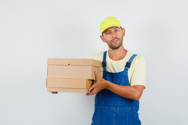 Young loader in uniform holding cardboard boxes , front view.