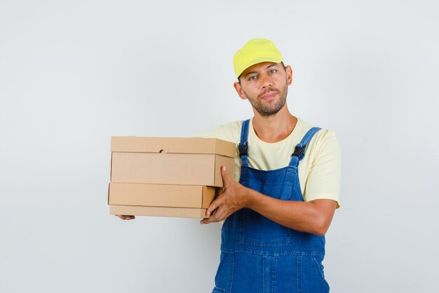 Young loader in uniform holding cardboard boxes , front view.