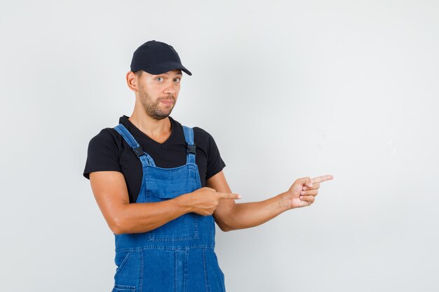 Young loader in uniform pointing to side , front view.