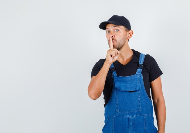 Young loader in uniform showing silence gesture and looking careful , front view.