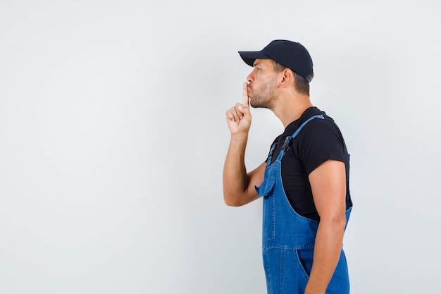 Young loader in uniform showing silence gesture and looking careful .