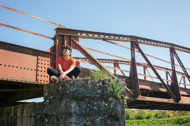 Free photo young lonely male hiker sitting near bridge