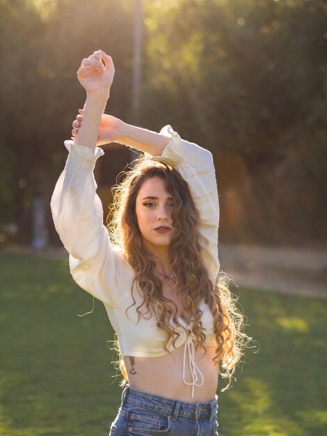 Молодая длинноволосая испанка позирует в весеннем парке с поднятыми руками