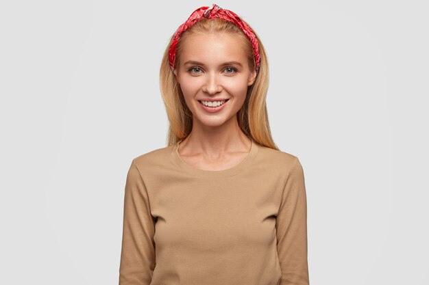 Young lovely blonde woman smiling, long hair, wears headband and beige casual sweater, expresses positive emotions