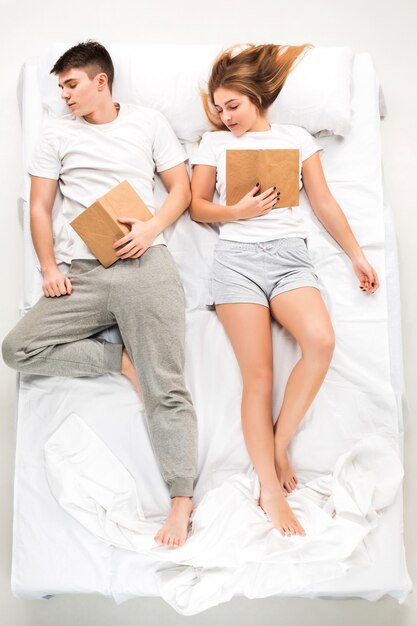 Молодая милая пара, лежа в кровати с книгами