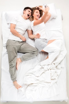 La giovane coppia adorabile che si trova in un letto con il telefono, amore lconcept, vista dall'alto