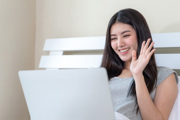 Young lovely woman sitting and smiling on bed and using laptop with joyful