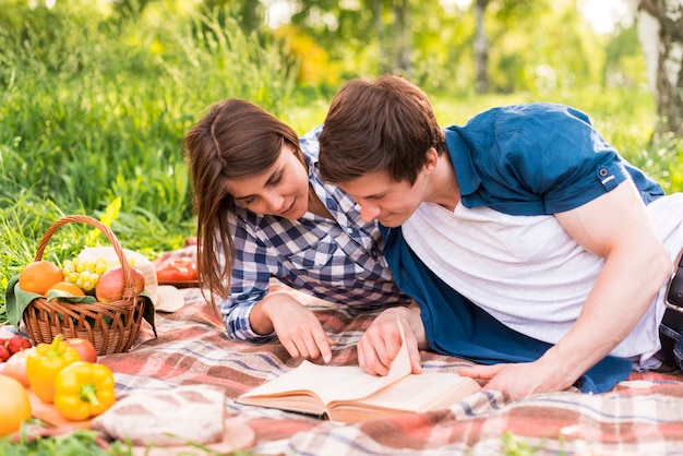 Free photo young lovers reading book on blanket outside