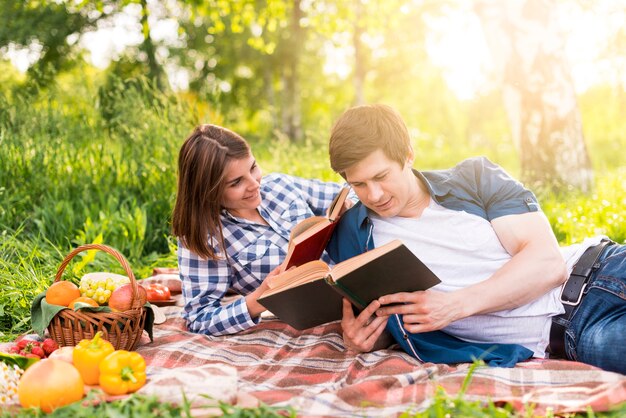 Young lovers resting on plaid and reading books