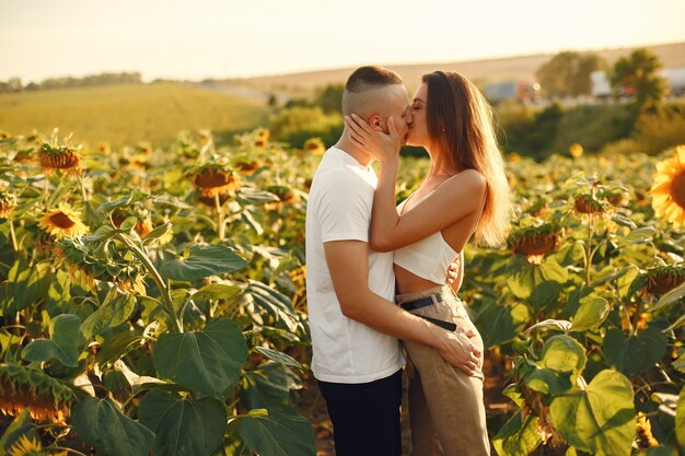 ひまわり畑で若い夫婦がキスします。フィールドで夏にポーズのカップルの肖像画。