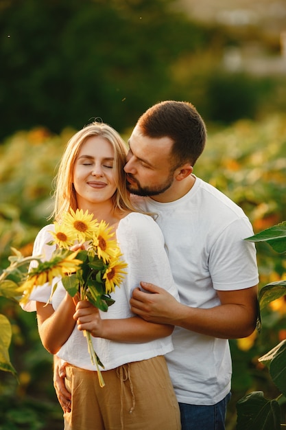 Young loving couple is kissing in a sunflower field. Portrait of couple posing in summer in field.