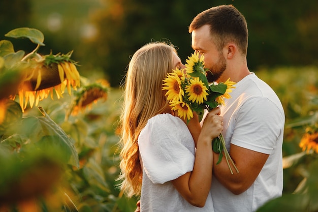 ひまわり畑で若い夫婦がキスします。フィールドで夏にポーズのカップルの肖像画。