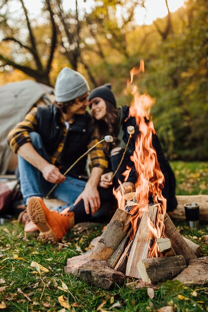 Young loving couple of tourists relaxing near the fire in the nature