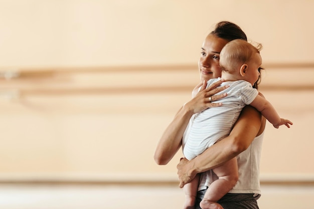 Free photo young loving mother holding her baby boy while taking a break from exercising in a health club copy space