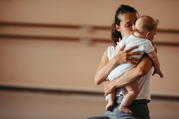 Foto gratuita giovane madre amorevole che bacia il suo bambino mentre lo tiene durante la lezione di esercizio nel club benessere copia spazio