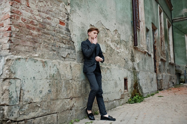 Молодой мачо в стильной черной куртке курит сигарету на улице