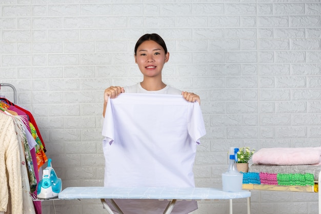 A young maid who is preparing a shirt on her ironing board with a white brick .