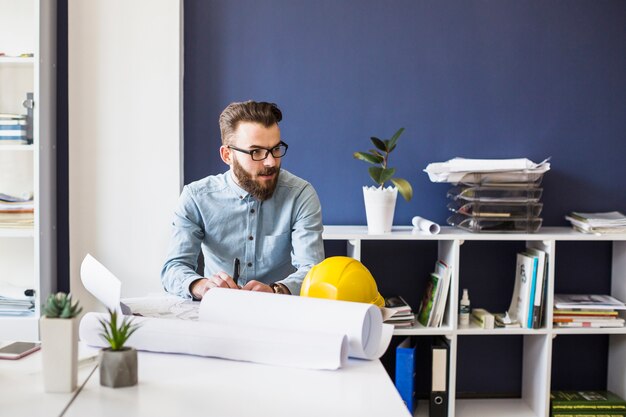 Young male architect with blueprint on table at workplace