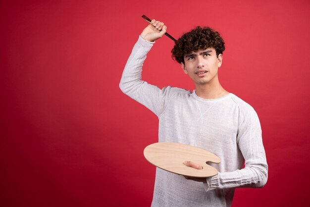 Young male artist holding palette and brushes  .