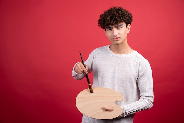 Young male artist looking at camera with painting tools.