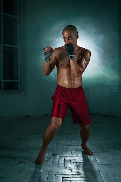 Free photo the young male athlete kickboxing on a background of blue smoke
