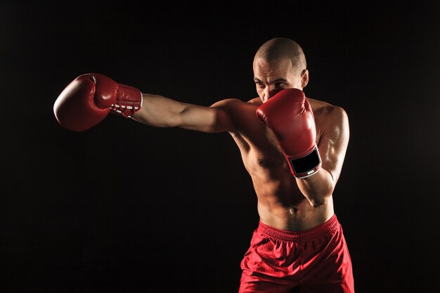 The young male athlete kickboxing on a black background